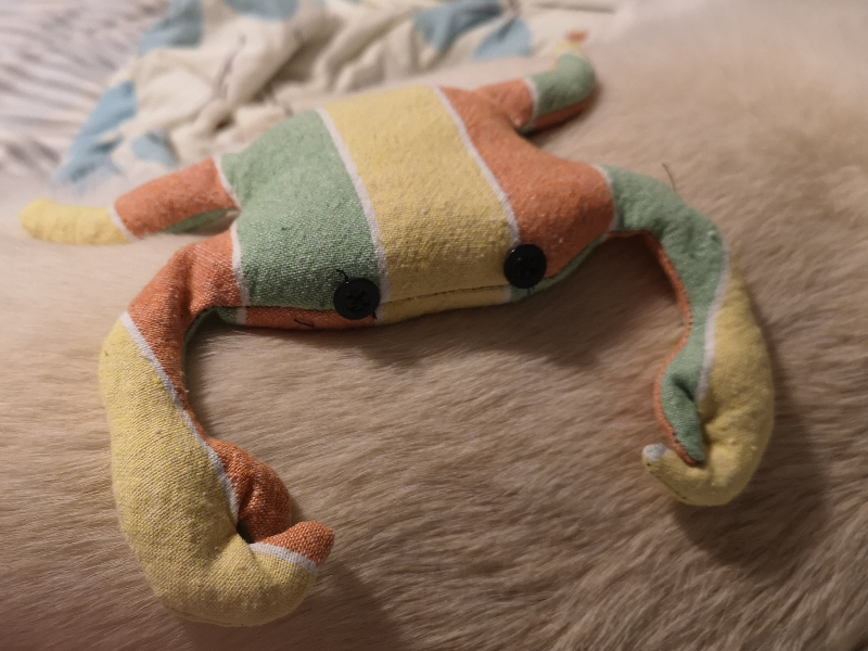a beanbag crab made of green, yellow, and orange striped fabric with black buttons for eyes